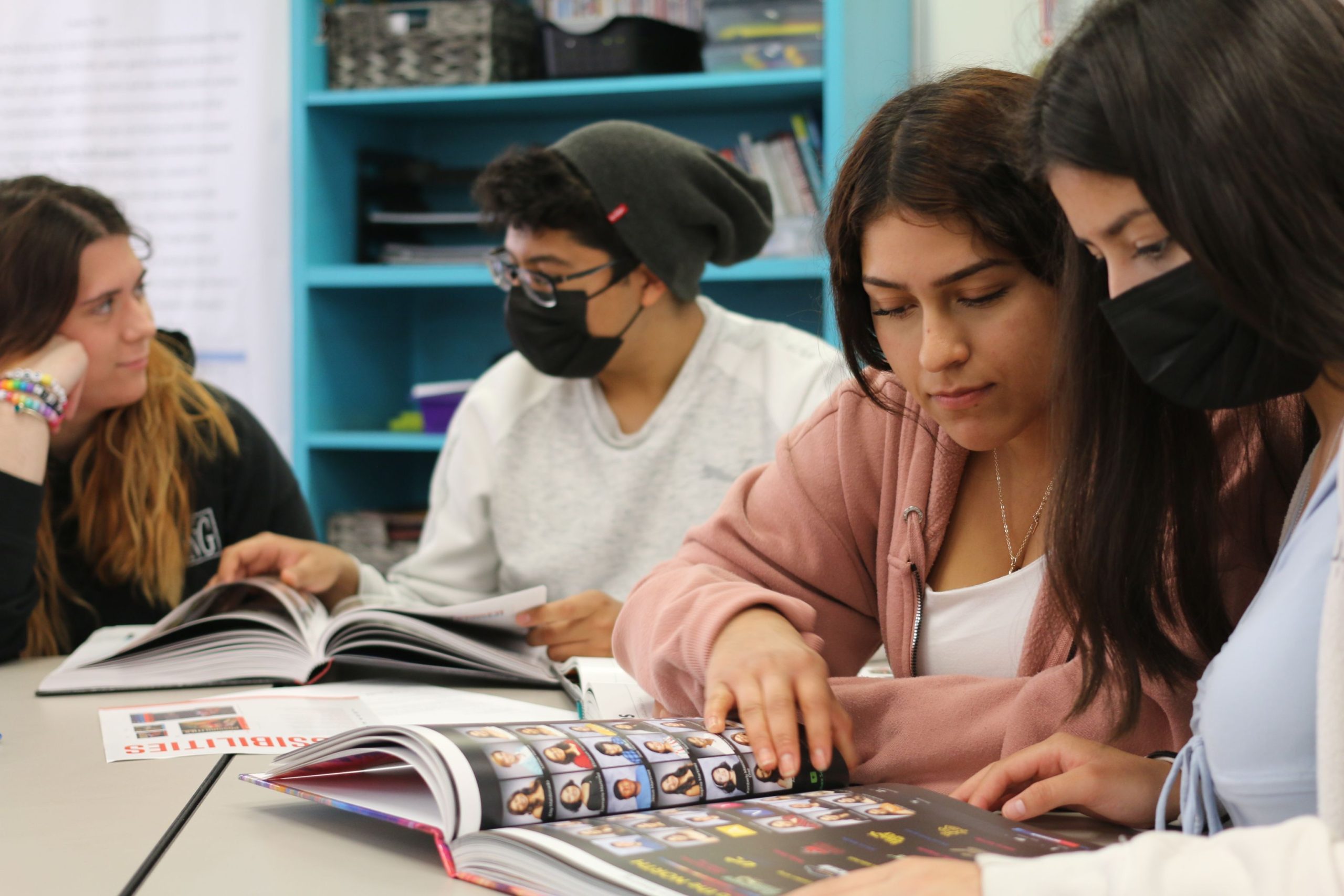 Students sitting at a table and looking at the yearbook. Some students are masked.