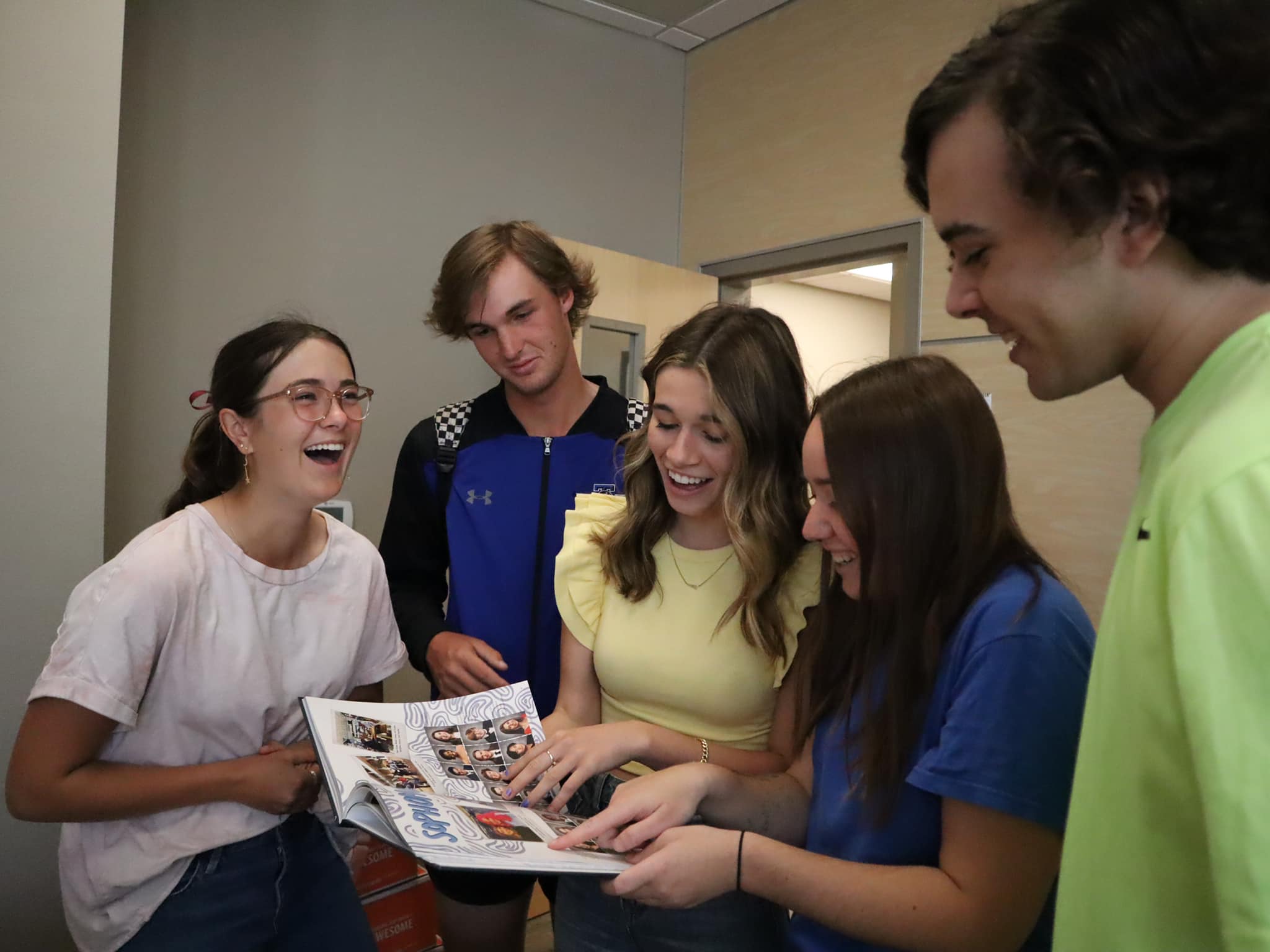 A photo of multiple students surrounding a yearbook and smiling