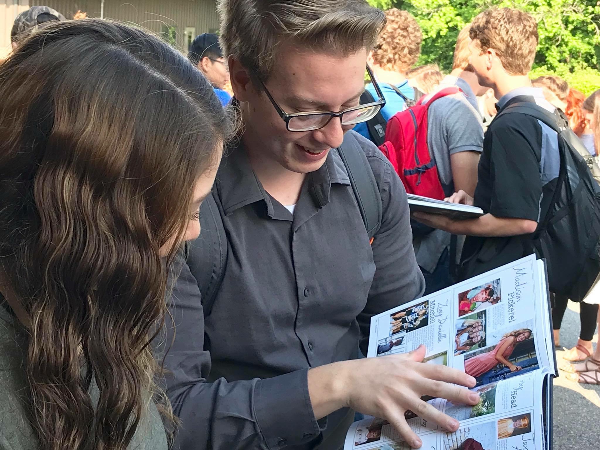Two people lean their heads over the open pages of a yearbook.