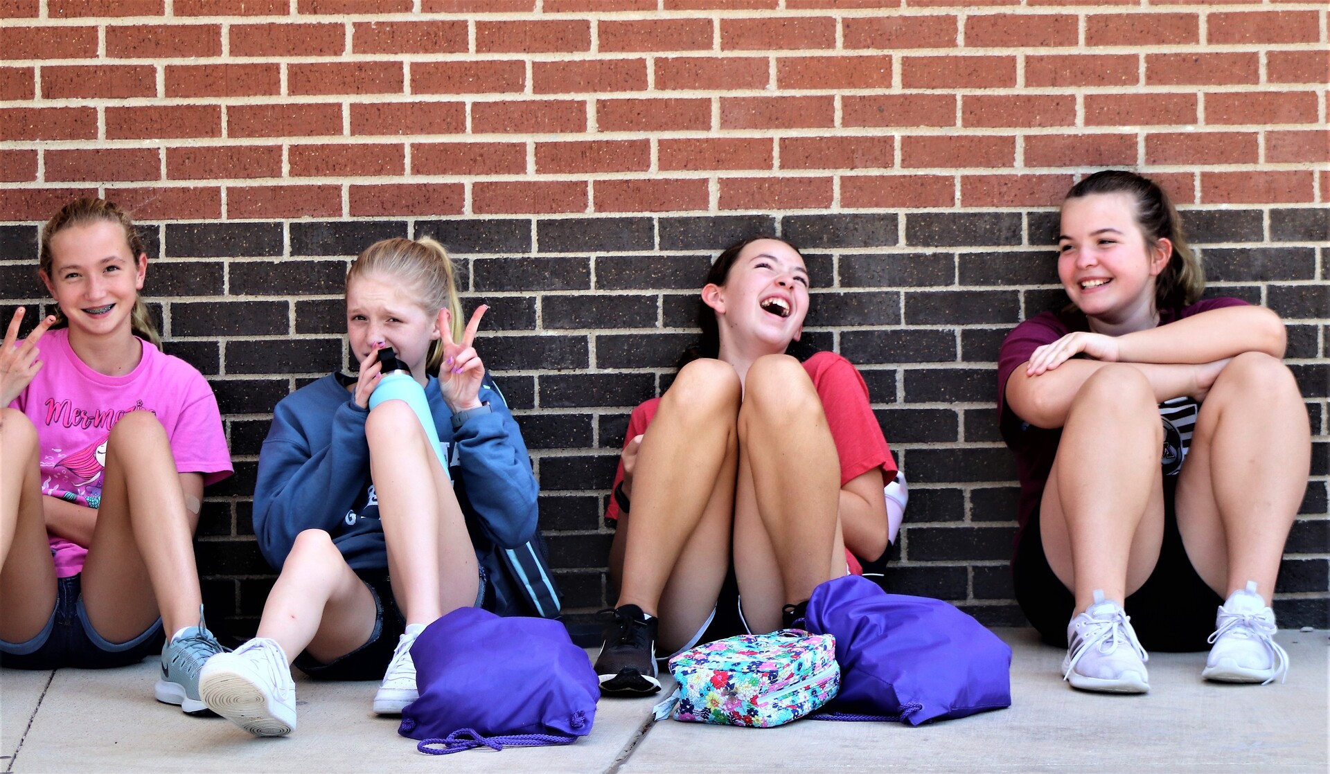 Four young girls sitting against a brick wall, smiling and laughing
