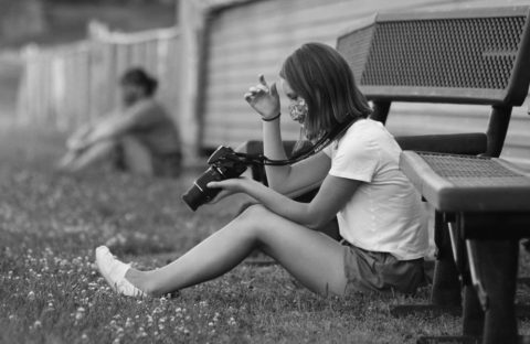 A student sitting in the grass with her camera reviewing a photo she just took. 