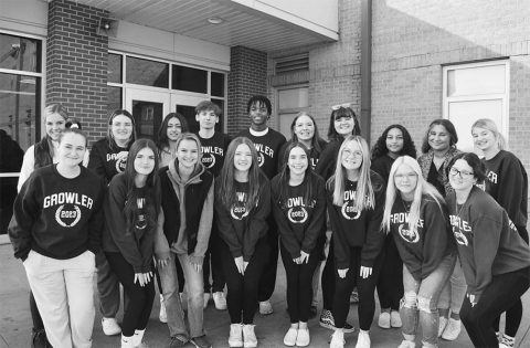 A group of about 20 yearbook students pose in front of a school. 