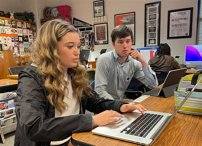 Aledo High School yearbook editor-in-chief Bridget Battenfield shows Tripp Walsworth their cover design as they both sit at a desk looking at a laptop. 